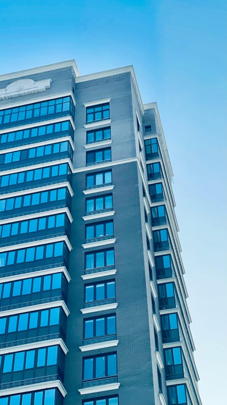 Vertical view of a contemporary high-rise building with reflective windows under a clear blue sky.