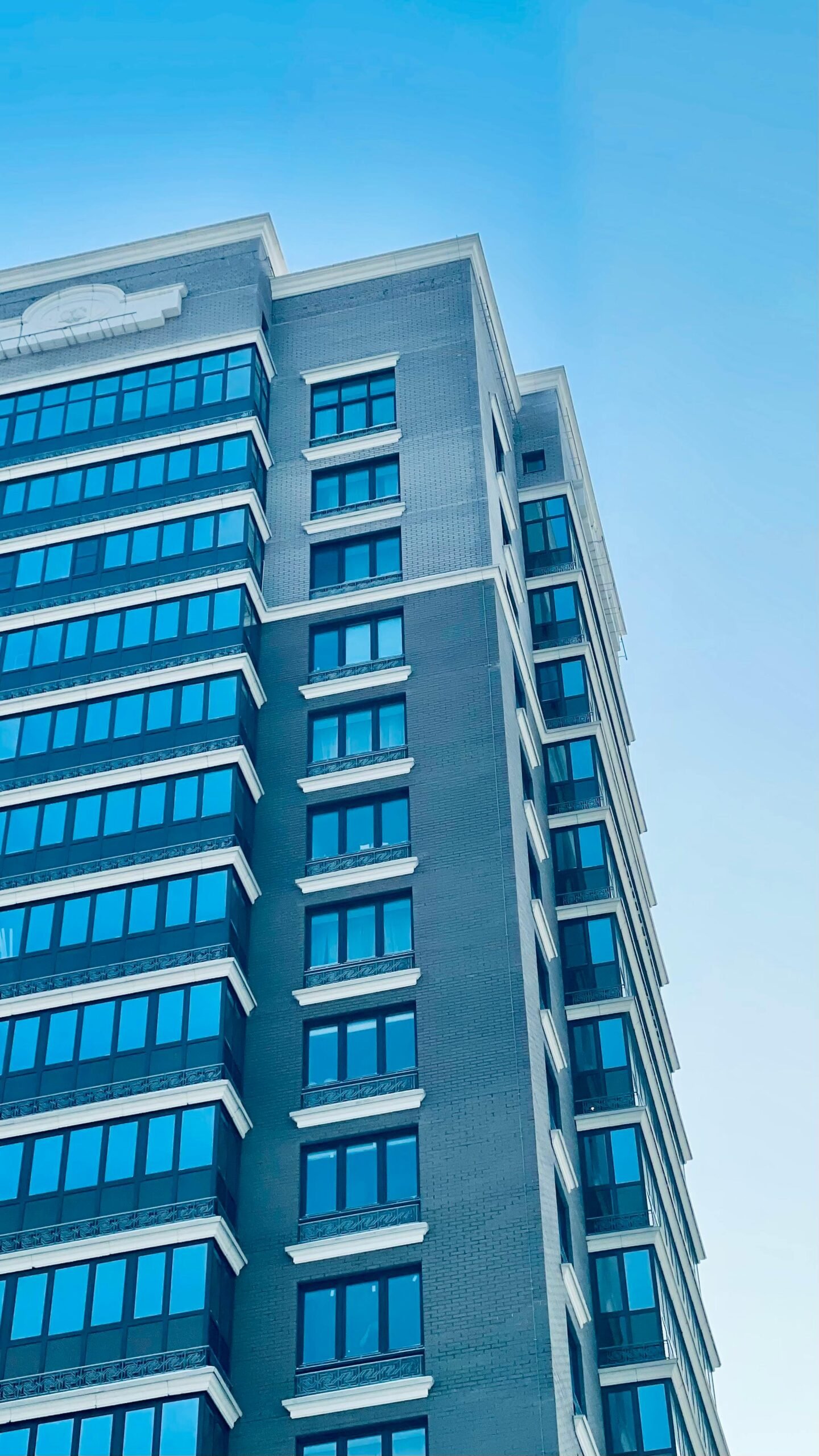 Vertical view of a contemporary high-rise building with reflective windows under a clear blue sky.